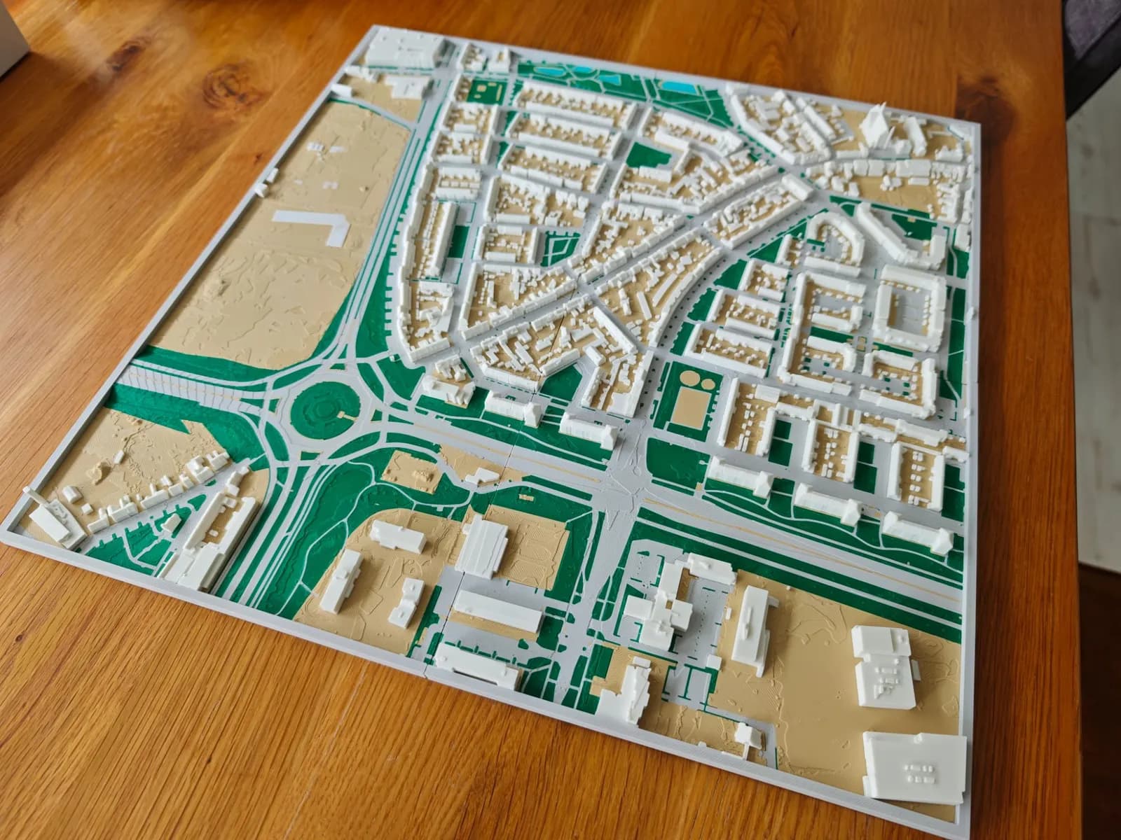 Dezelfde vier tegels tegen elkaar gelegd als één 3D-geprinte stadskaart van 40 × 40 cm, met een rotonde, woonwijken en groen die over de naden doorlopen