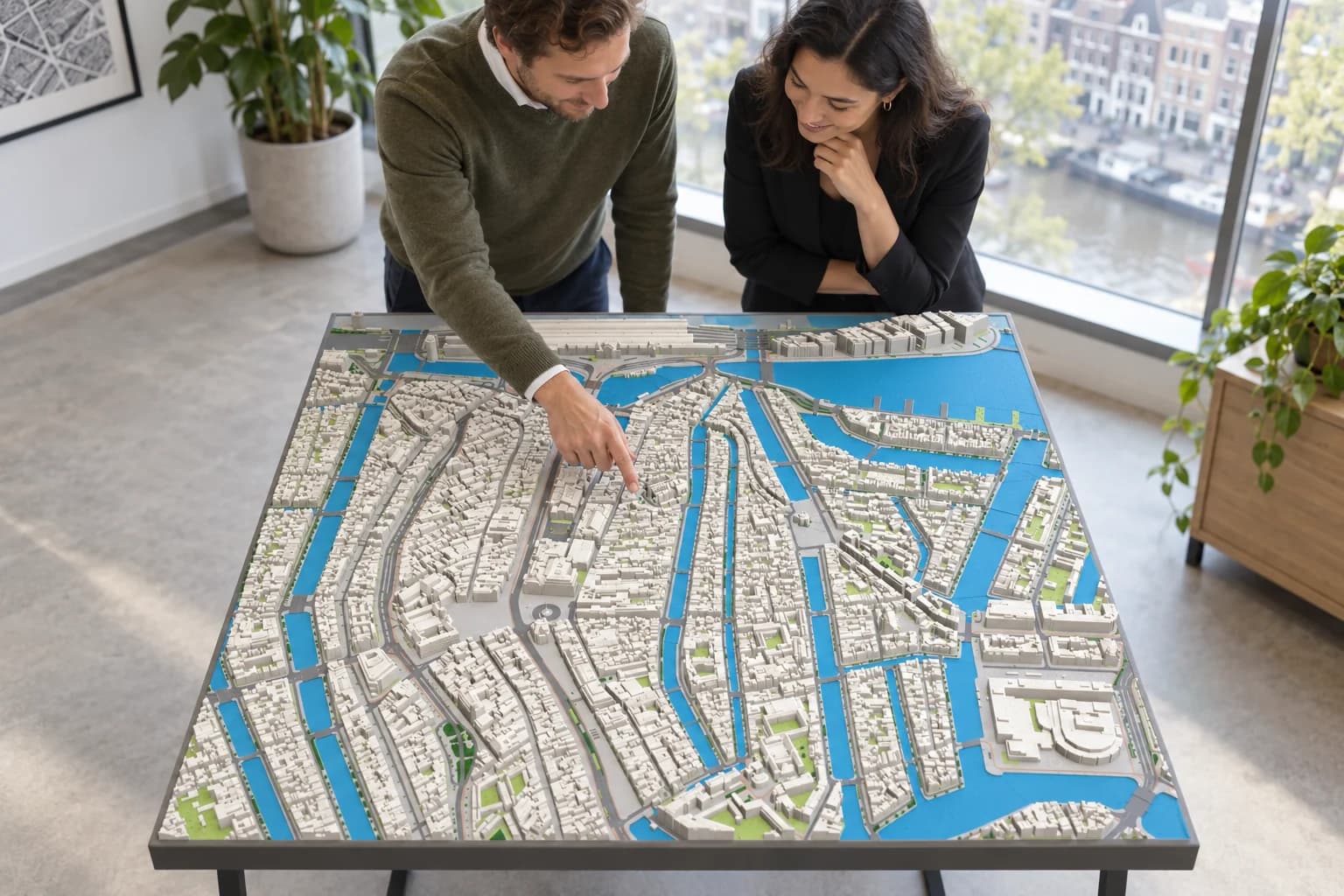 Twee mensen bekijken een 3D-geprinte maquette van het centrum van Amsterdam die het hele tafelblad vult; een van hen wijst een buurt in de grachtengordel aan