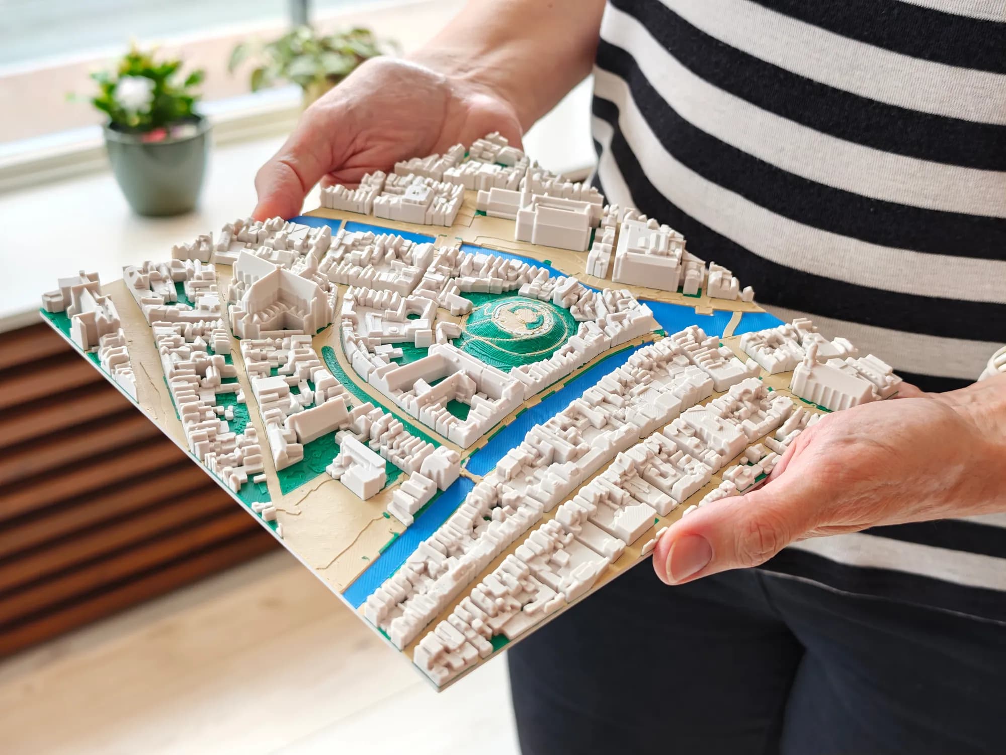 3D-geprinte stadskaart van het centrum van Leiden van 20 × 20 cm op schaal 1:2000, met de Burcht, grachten en dicht bebouwde straten, in twee handen gehouden