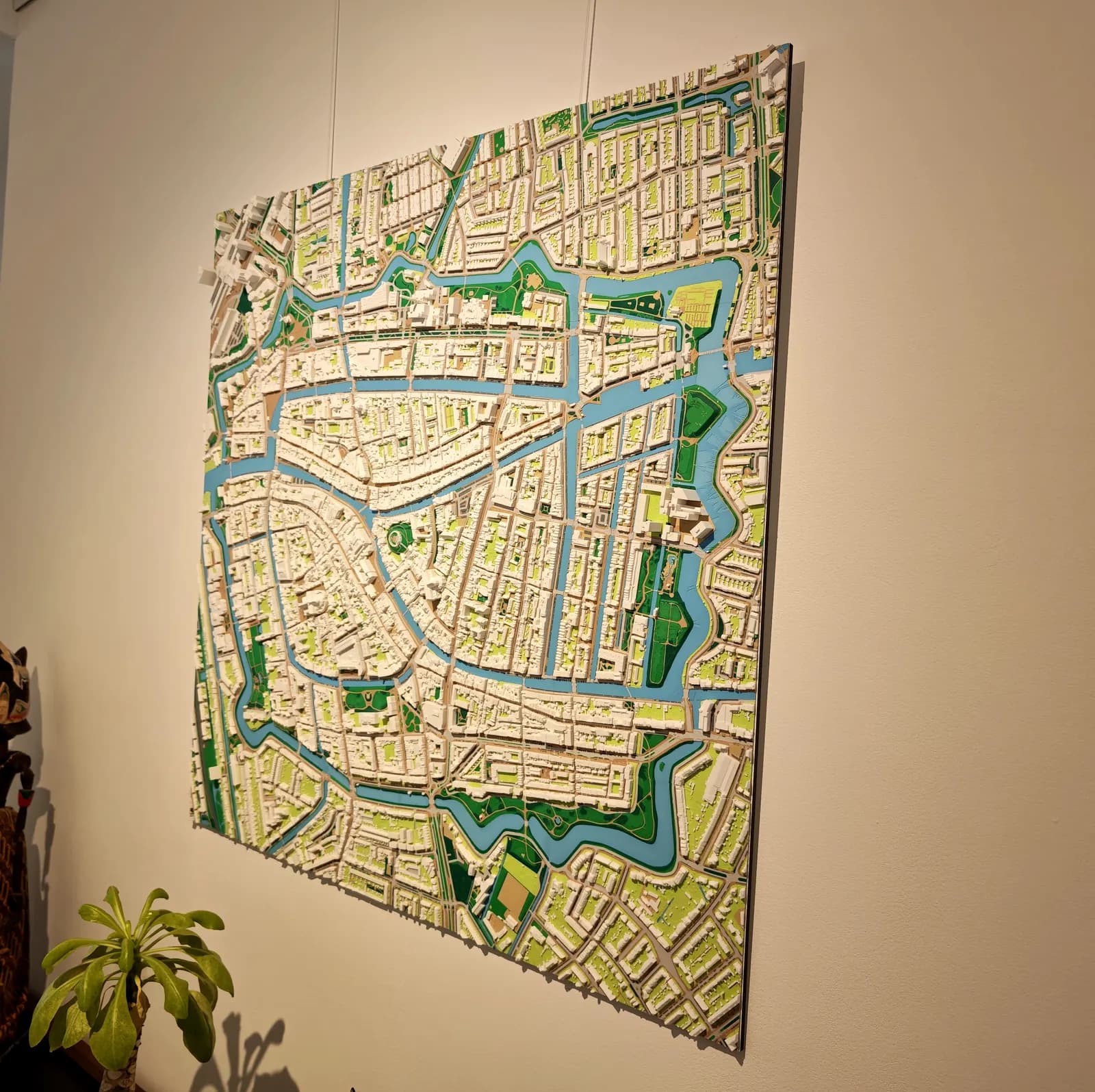 Samengestelde 3D-geprinte stadskaart van het centrum van Leiden van 80 × 80 cm op schaal 1:2250, met de singels en grachten in blauw en veel groen, aan de muur gehangen