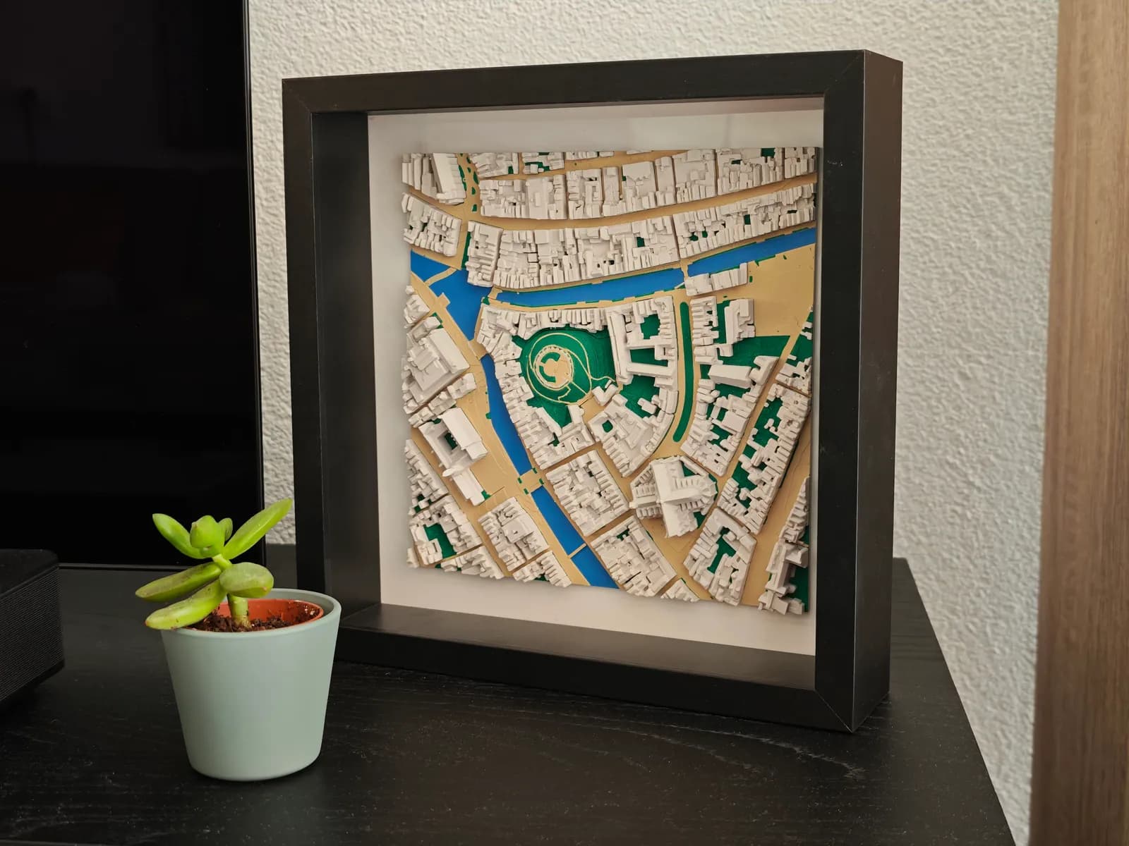 3D-geprinte stadskaart van 20 × 20 cm in een diepe zwarte fotolijst op een kast, naast een plantje