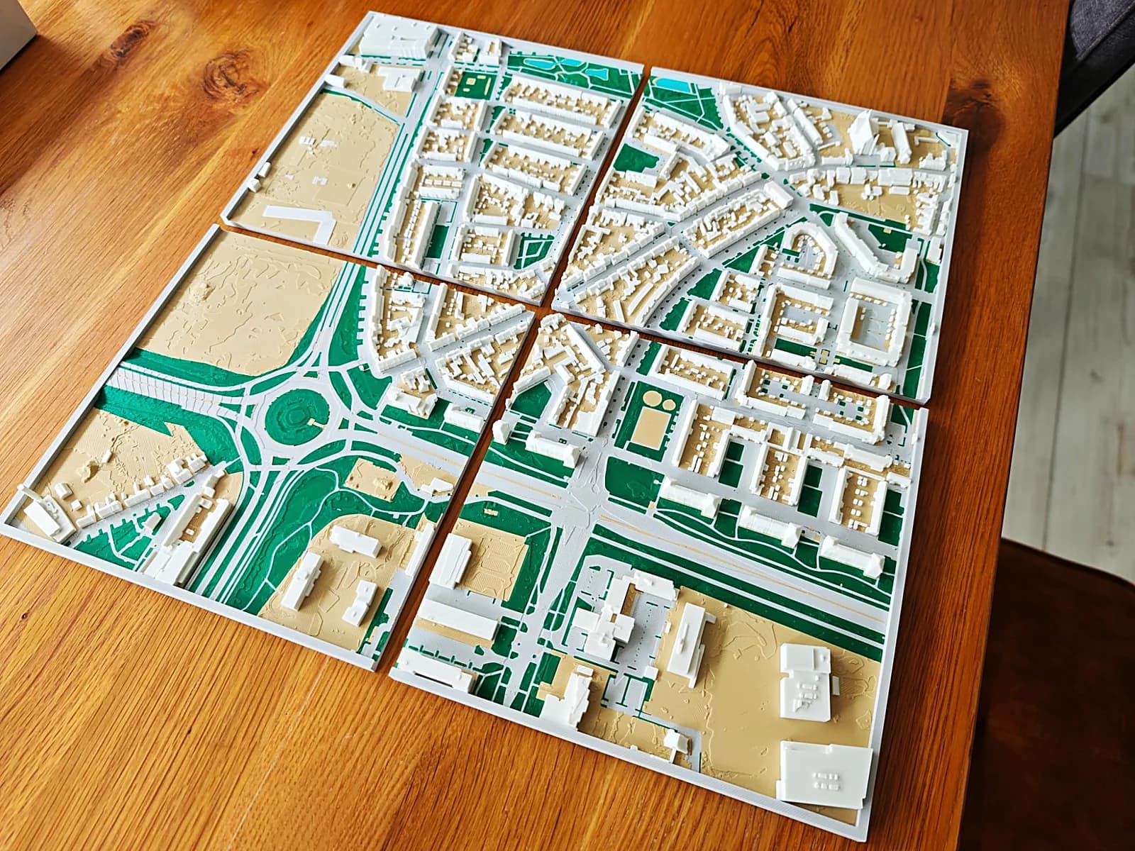 Vier 3D-geprinte tegels van de omgeving van de Hasseltstraat in Tilburg iets uit elkaar gelegd, met een rotonde, woonwijken en groen